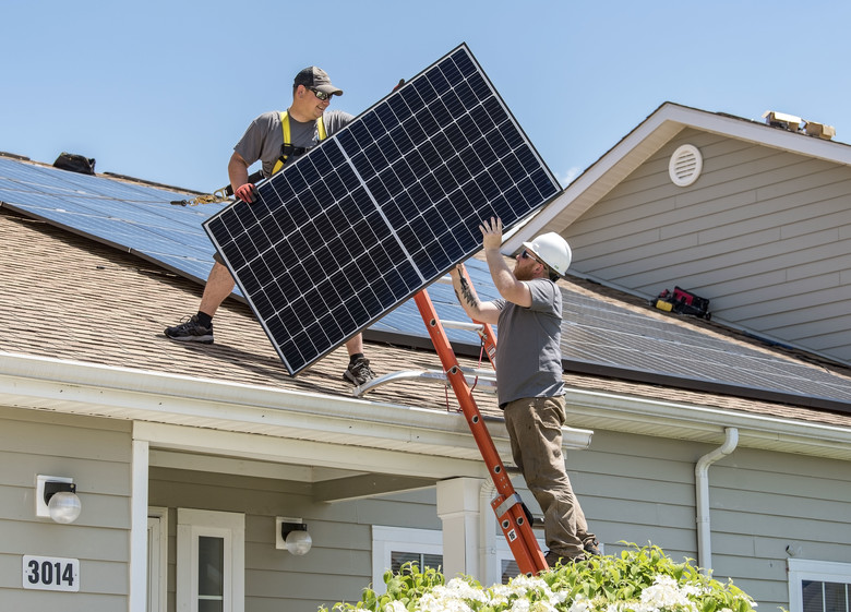 Wyatt Whelan, left, and Eric Roberts, both PosiGen install supervisors, move a photovoltaic (PV) panel to a roof May 11, 2018, in the Dover Family Housing community at Dover Air Force Base, Del. Depending on the size of the housing unit, installation of the PV panels generally takes three to five days. (U.S. Air Force photo by Roland Balik)